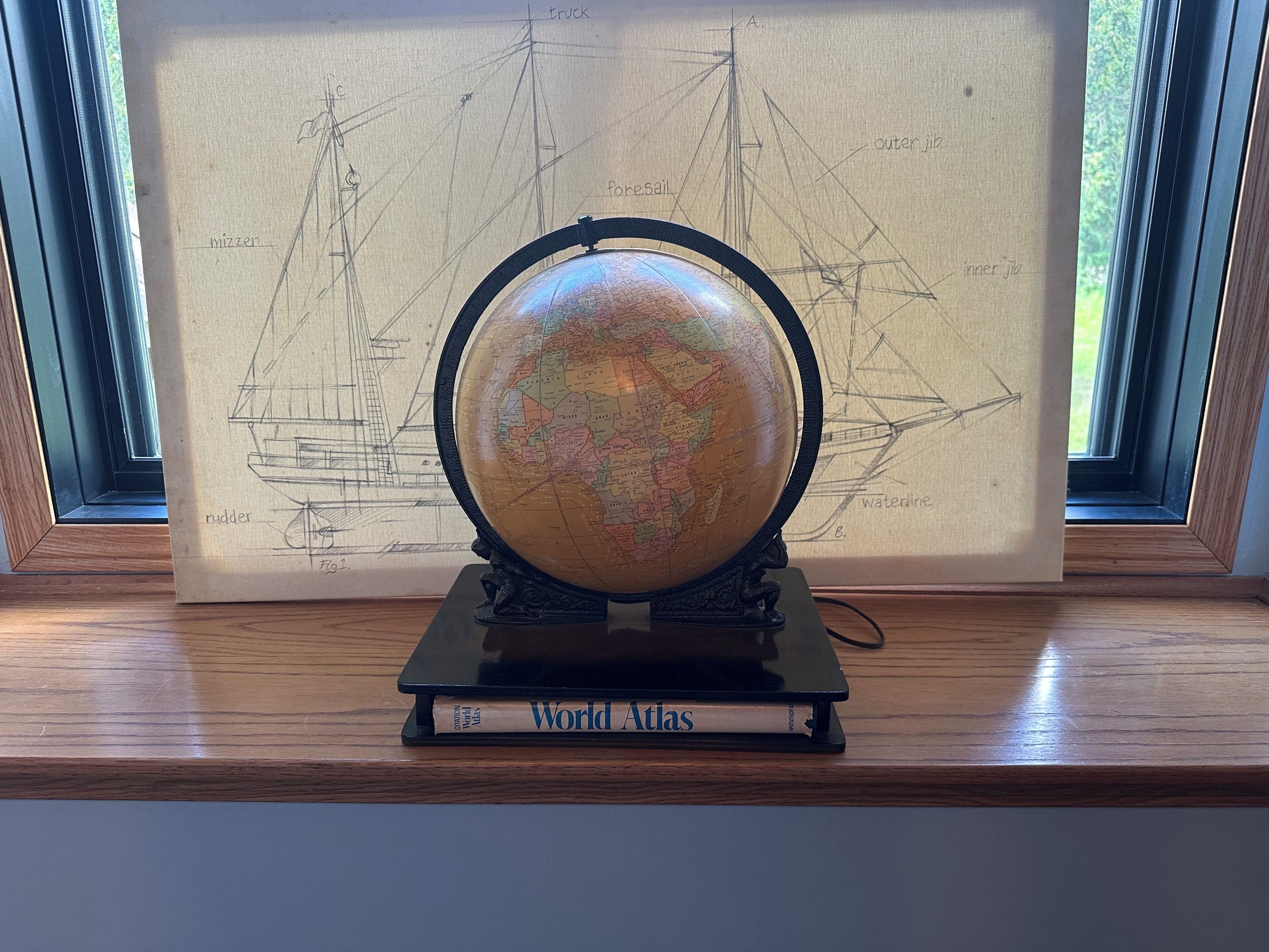 A globe on a stand with a framed ship diagram behind it, placed on a wooden shelf.