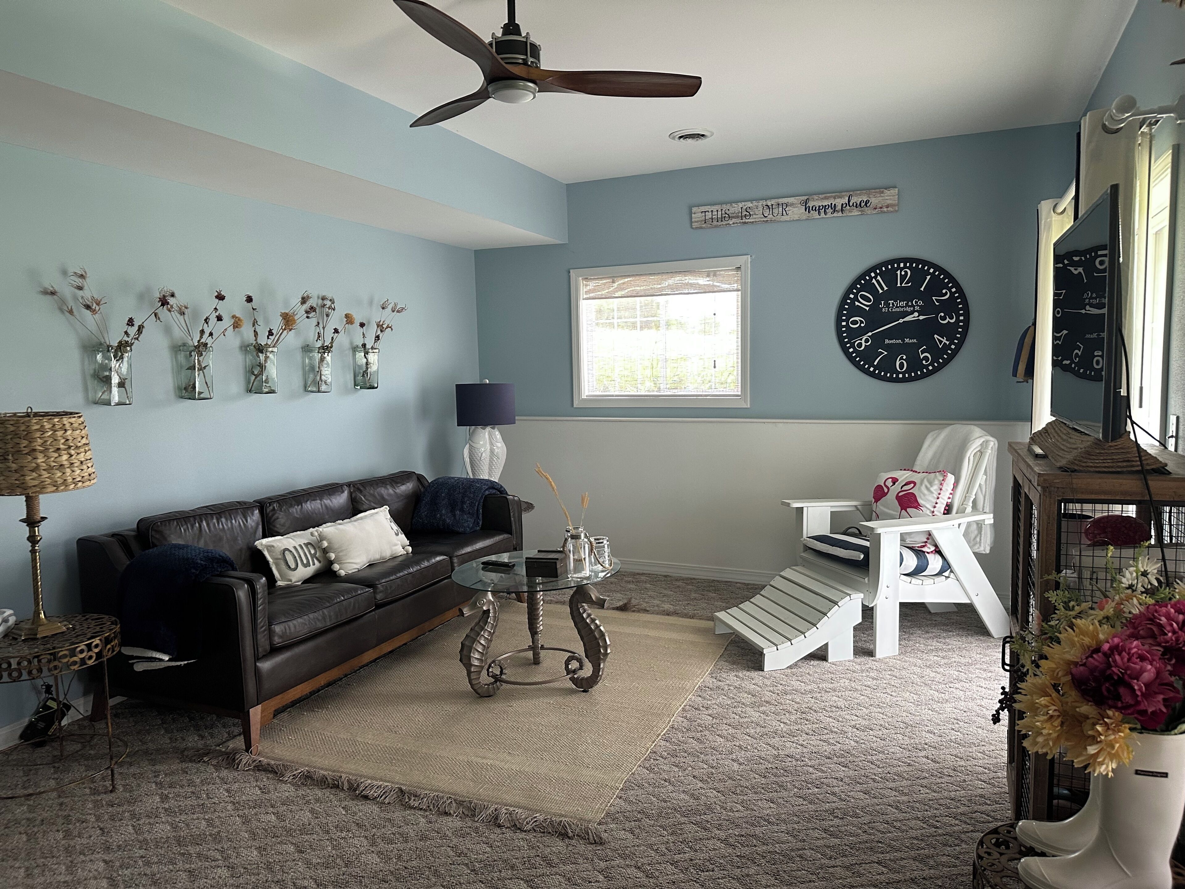 A living room with a ceiling fan, a clock, a sofa, a coffee table, and a window with blinds.