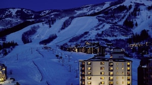Una montaña nevada con un telesilla y edificios con ventanas iluminadas.