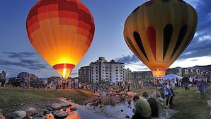 Un festival de globos aerostáticos con numerosos globos, una multitud de personas y un edificio al fondo.