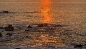Un capvespre sobre un mar tranquil amb roques al primer pla.