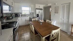A modern kitchen with white cabinets, a stainless steel refrigerator, a microwave, and a dining table with chairs. - Delightful and trendy 1 bedroom -1 bath condo F403 (Marco Island)