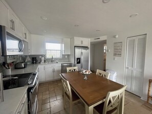 Una cocina moderna con armarios blancos, un refrigerador de acero inoxidable, un microondas y una mesa de comedor con sillas.
