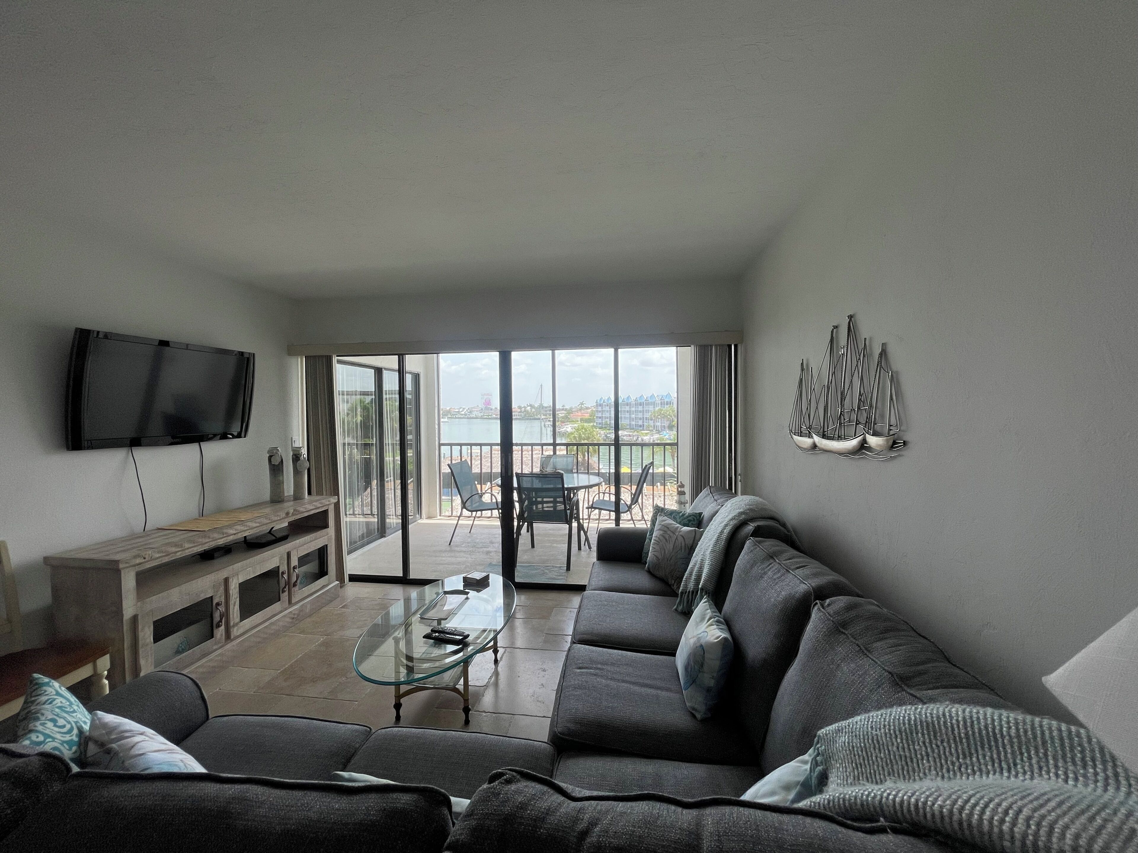 Een woonkamer met een bank, een glazen salontafel, een televisie en een balkon met uitzicht.