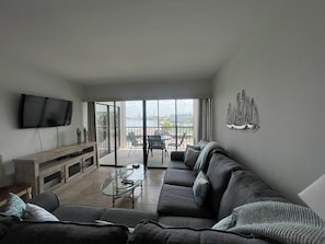 Una sala de estar con sofá, una mesa de centro de vidrio, televisor y un balcón con vistas.