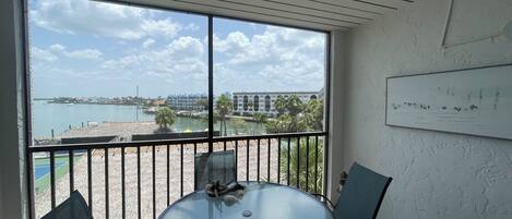 A room with a round glass table and two chairs, a view of a marina and buildings across the water, and a ceiling with a light fixture.