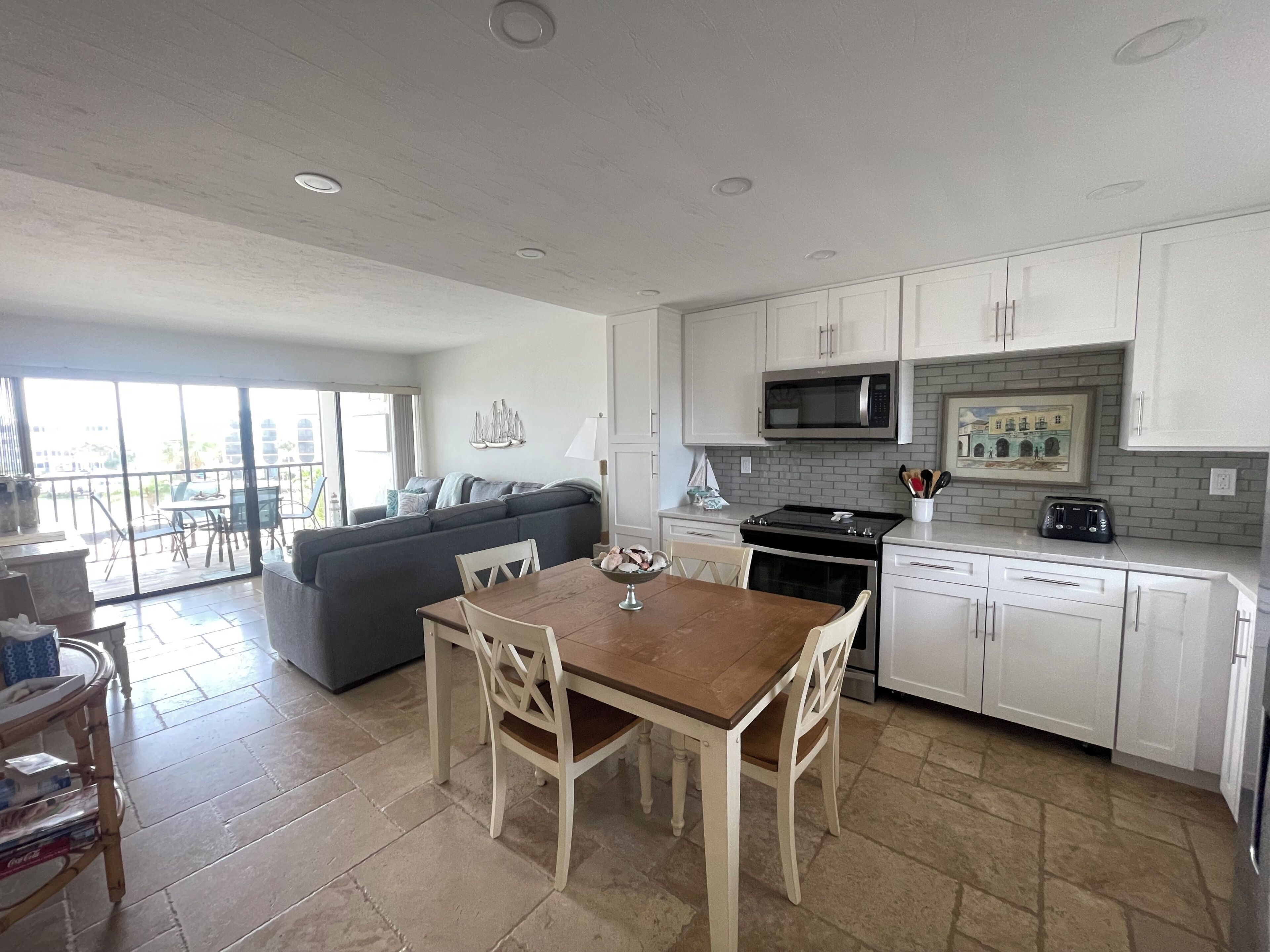 A modern kitchen with white cabinets, a dining table, and a gray sofa.