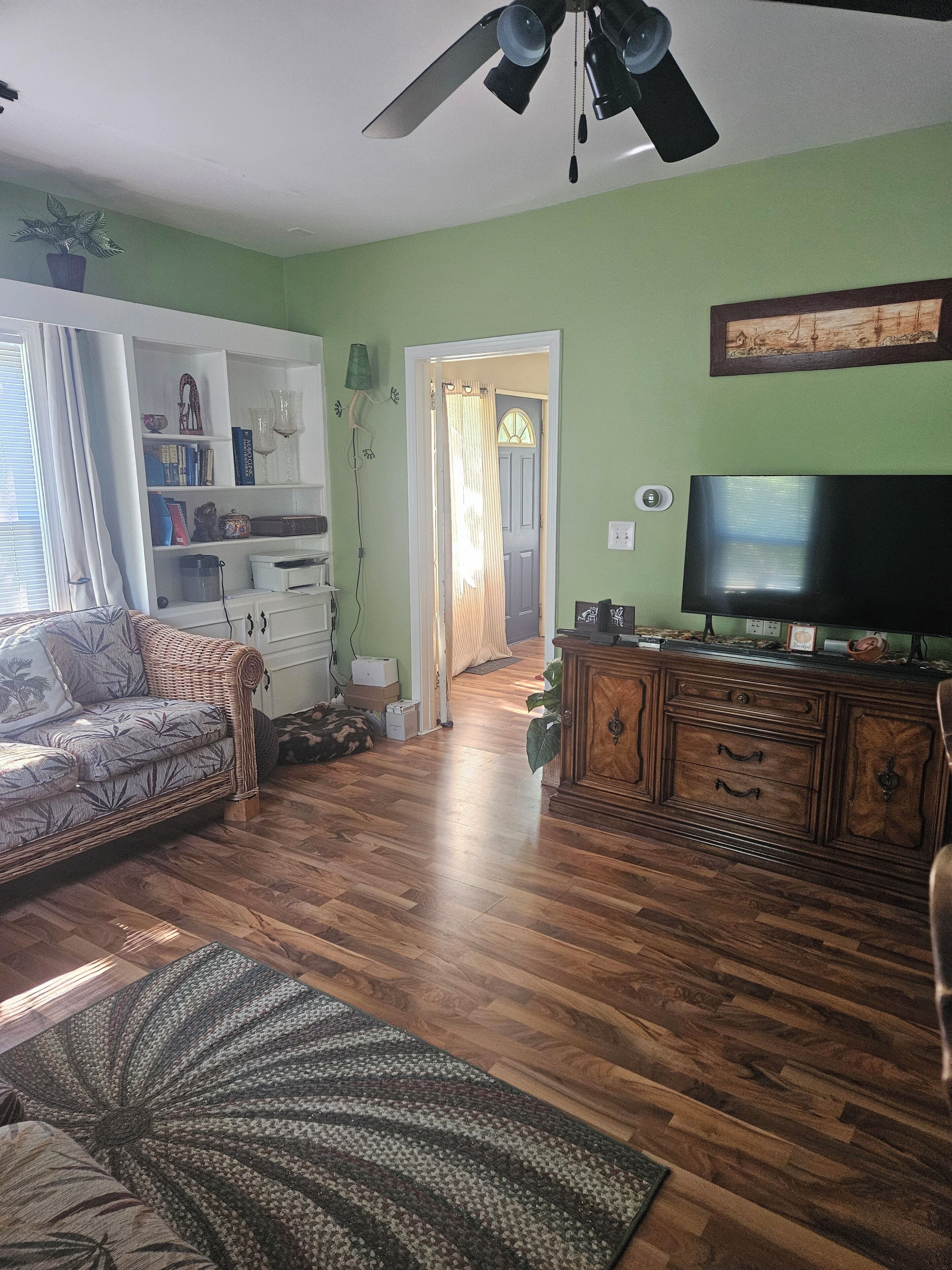 A living room with a sofa, a television, a wooden cabinet, and a ceiling fan.