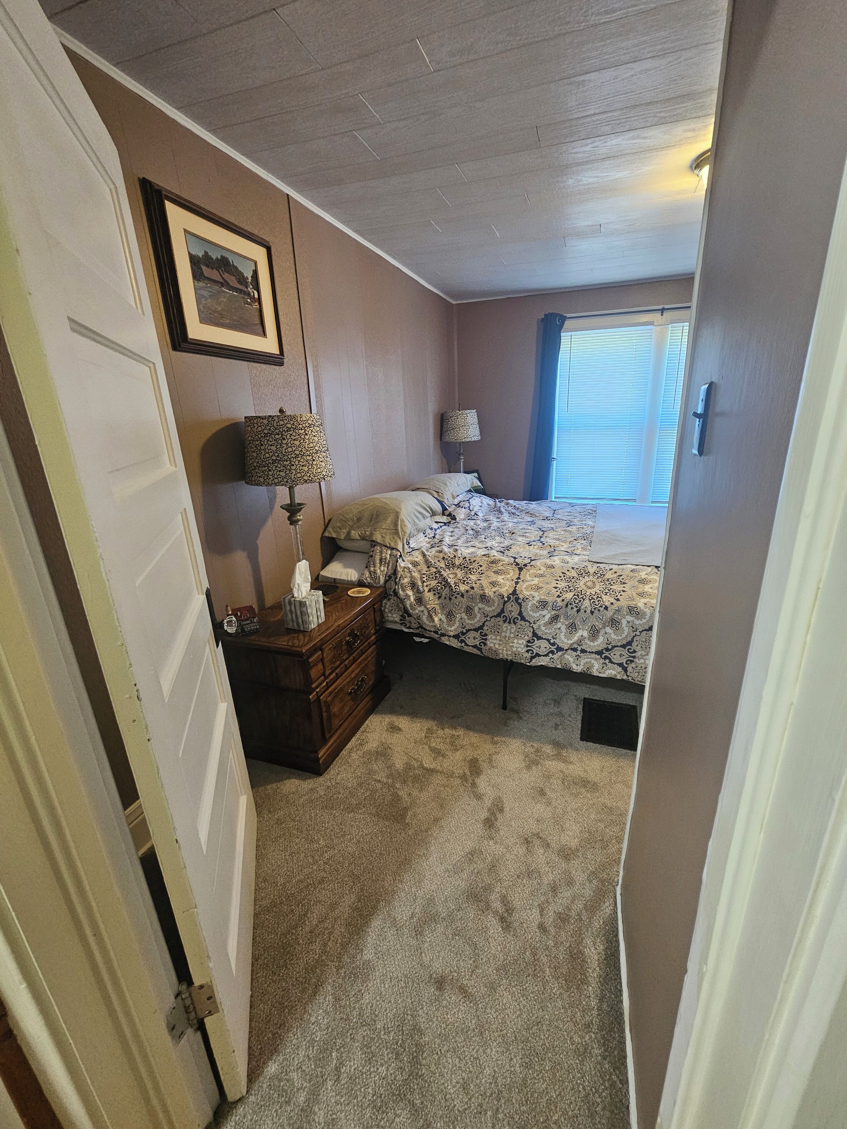 Ein Schlafzimmer mit Bett, Kommode, Lampe und einem Bild an der Wand.