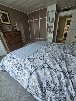 Ein Schlafzimmer mit Bett, Kommode, Kleiderschrank und Bücherregal.