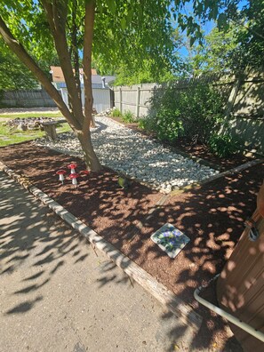 A garden area with a tree, a wooden fence, and a paved path. - Serene 4-bedroom house with AC in Spring Lake with old fashioned charm. (Spring Lake)