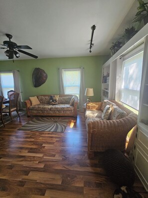A living room with two wicker sofas, a ceiling fan, and a large window with blinds. - Serene 4-bedroom house with AC in Spring Lake with old fashioned charm. (Spring Lake)