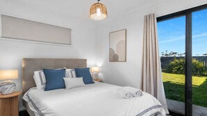 A modern hotel room with a large bed, two bedside tables, a wall-mounted artwork, and a view of the outdoors. - Beach Street Studio Vincentia (Vincentia)