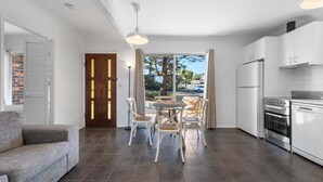 A modern kitchen with white cabinets, a dining table with chairs, and a gray sofa. - Beach Street Studio Vincentia (Vincentia)