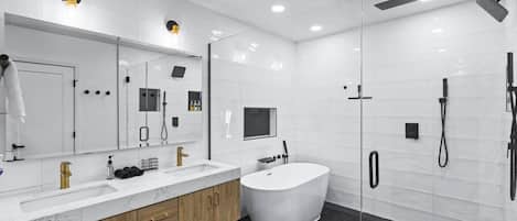 A modern bathroom with a large mirror, a freestanding bathtub, and a glass-enclosed shower area.