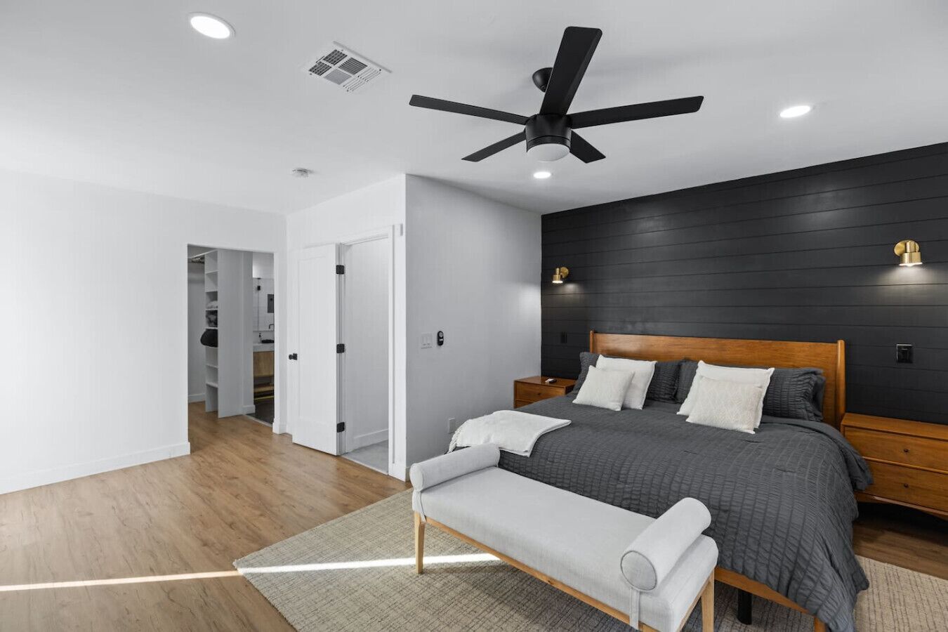 A modern bedroom with a bed, bedside tables, a bench, a ceiling fan, and a wardrobe.