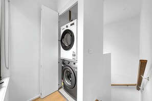 Un cuarto de lavado con lavadoras y secadoras apiladas, piso de madera y pared blanca.