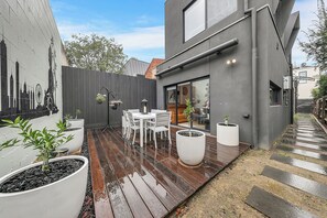 A modern outdoor patio with a wooden deck, white furniture, and potted plants. - Richmond Escape | 5BR | 3 Baths | Walk to MCG (Cremorne)