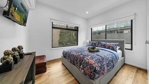 A bedroom with a bed, a dresser, a window, and a wall-mounted air conditioner. - Richmond Escape | 5BR | 3 Baths | Walk to MCG (Cremorne)
