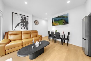 Ein modernes Wohnzimmer mit einer Ledersofa, einem Esstisch mit Stühlen, einem schwarzen Couchtisch, einer Wanduhr und einem flachbildfernseher über der Essecke.