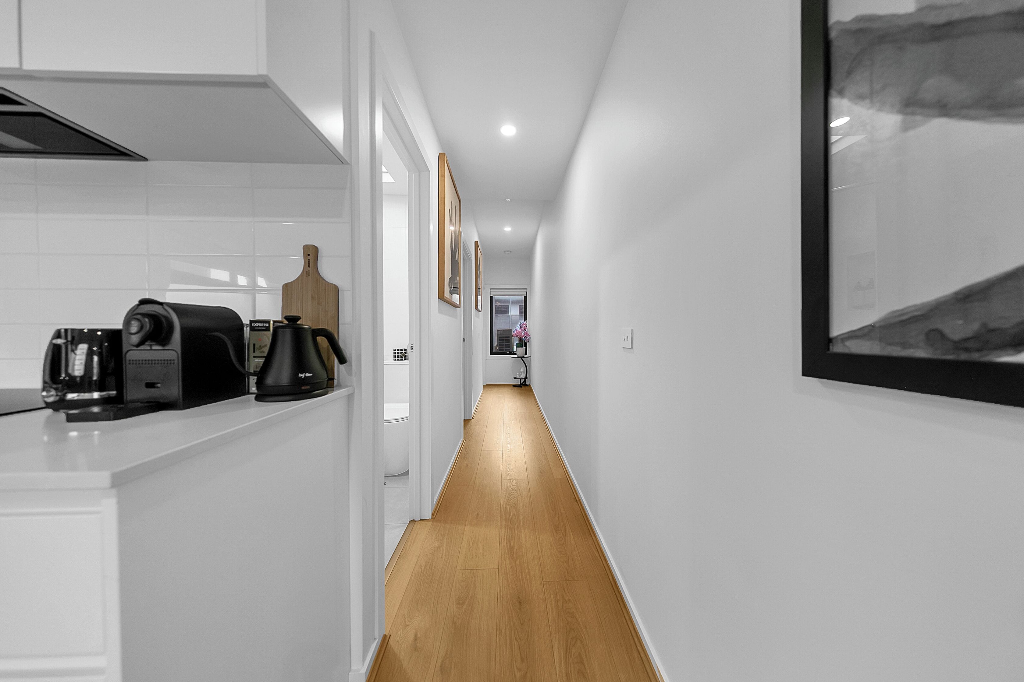 A narrow hallway with a kitchen area on one side, wooden flooring, and white walls.