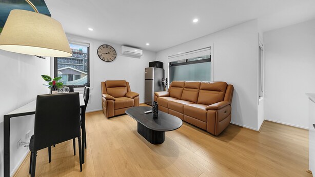 A modern living room with a sofa, two armchairs, a coffee table, and a dining area with a table and chairs. - Richmond Escape | 5BR | 3 Baths | Walk to MCG (Cremorne)