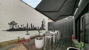 A patio with a white wall mural, a table with chairs, and potted plants. - Richmond Escape | 5BR | 3 Baths | Walk to MCG (Cremorne)