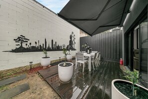 Eine Terrasse mit Wandgemälde in Weiß, einem Tisch mit Stühlen und Topfpflanzen.