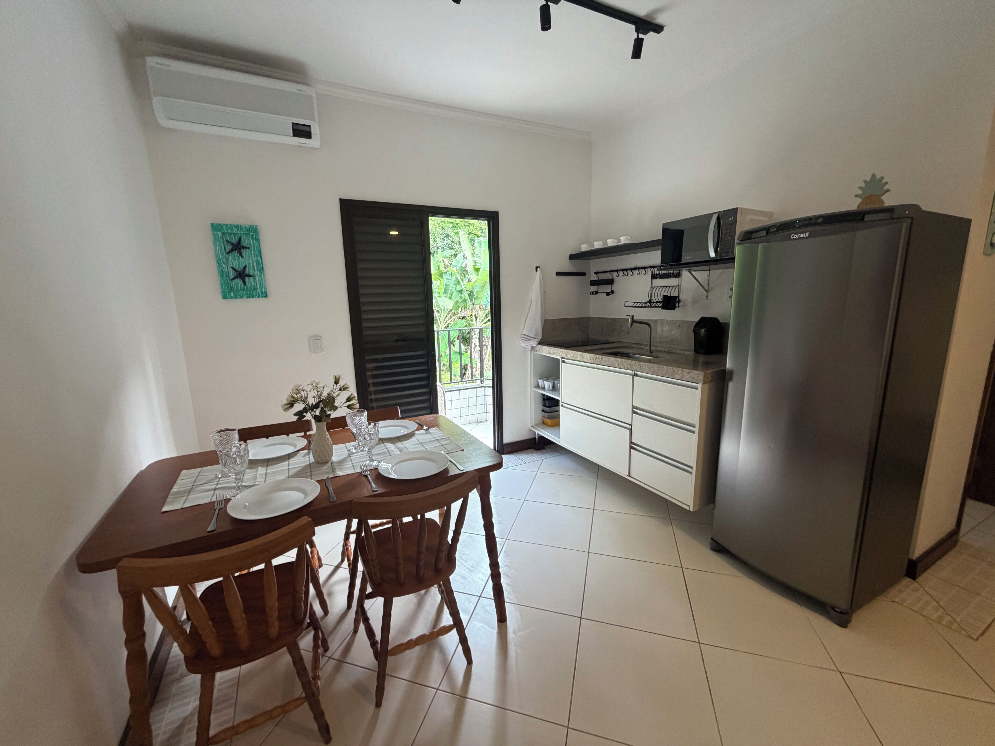 Une cuisine avec une table à manger pour quatre personnes, un réfrigérateur et une fenêtre donnant sur un paysage verdoyant.