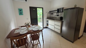 A kitchen with a dining table set for four, a refrigerator, and a window with a view of greenery. - Flat 38 Ubatuba Toninhas (Ubatuba)