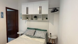 A bedroom with a bed, a wardrobe, a small table, and a hanging rack. - Flat 38 Ubatuba Toninhas (Ubatuba)