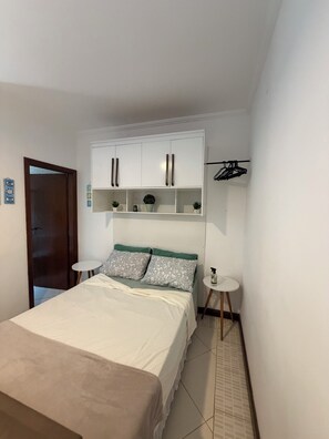 Ein Schlafzimmer mit einem Bett, einem Kleiderschrank, einem kleinen Tisch und einer Kleiderstange.