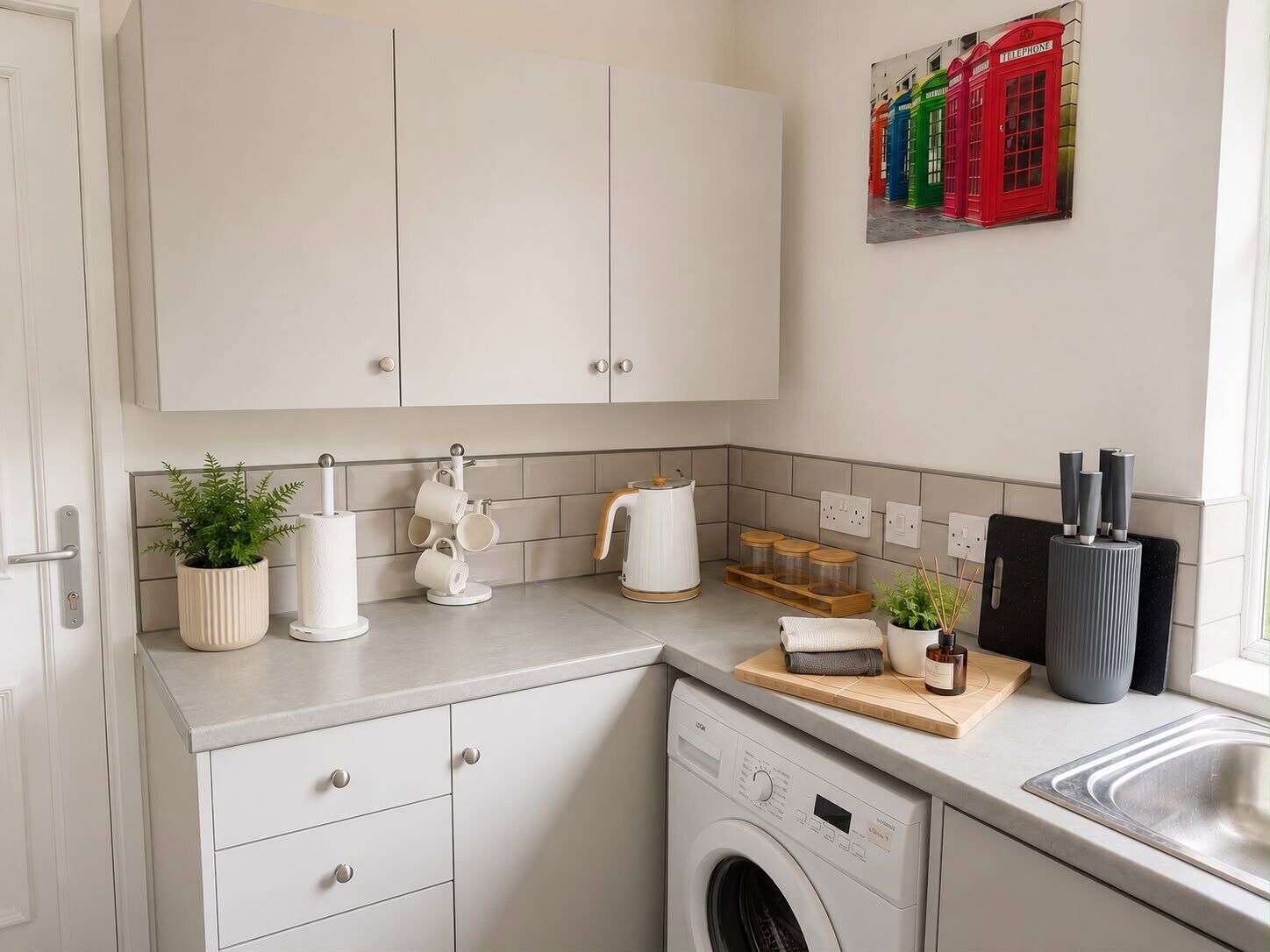 Une cuisine compacte équipée d’un lave-linge, d’une machine à café et d’une petite plante en pot.