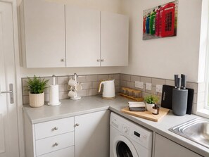 Eine kleine Küche mit Waschmaschine, Kaffeemaschine und einem kleinen Topfpflanzen.