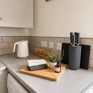 A kitchen counter with a kettle, jars, a cutting board, a plant, and a knife block. - Hartlepool 4BR Stay | Long Stay & Contractor Deals (Hartlepool)