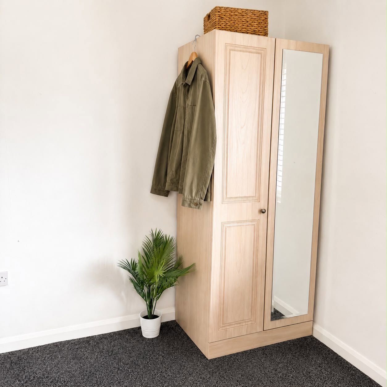 A wooden wardrobe with a mirror, a hanging jacket, and a potted plant.