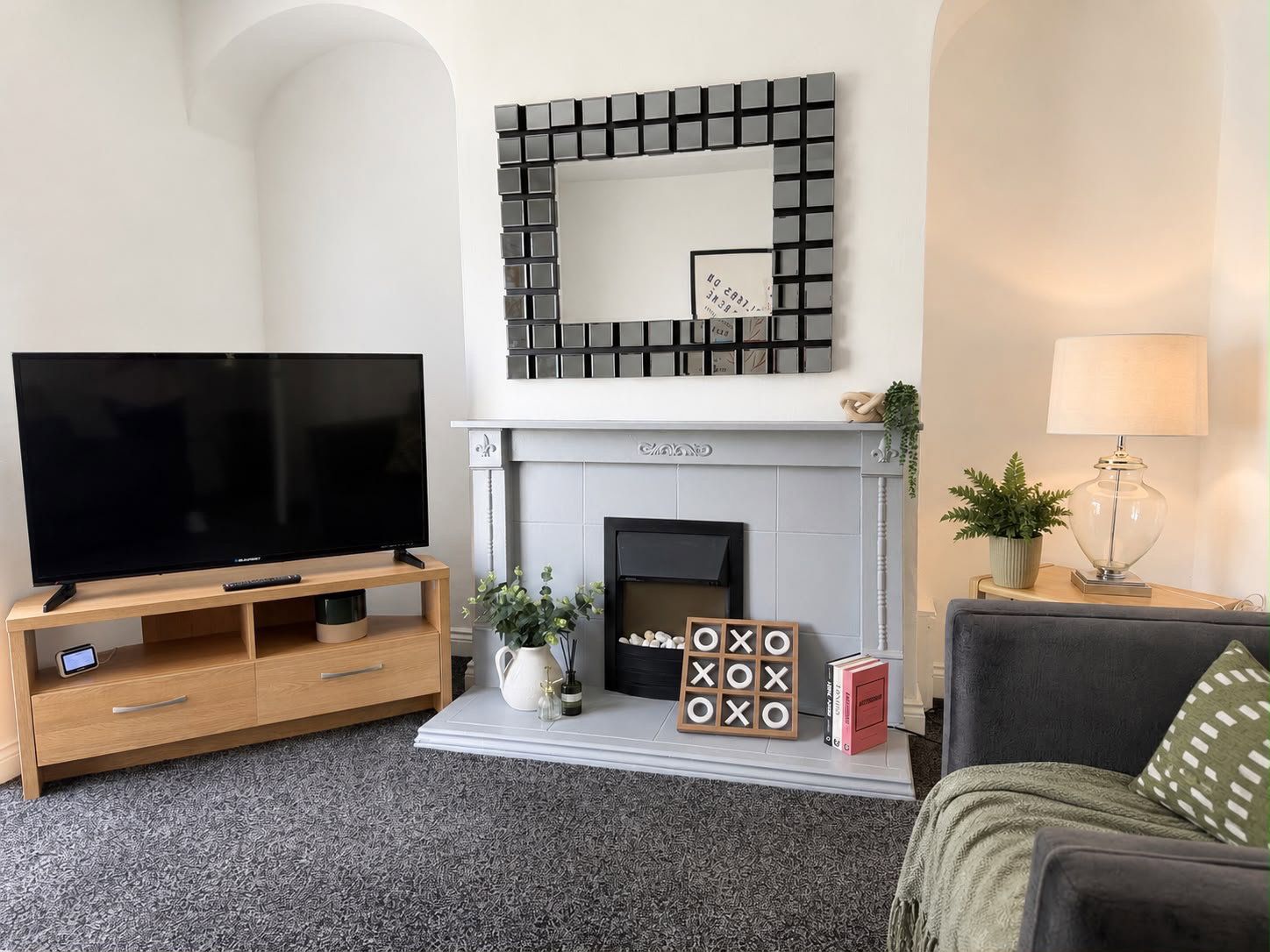 A living room with a flat-screen TV, a fireplace, a mounted mirror, and a sofa.