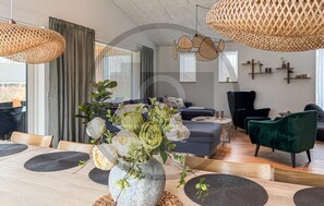A modern living room with a dining area, featuring a stone vase with flowers, woven light fixtures, and a dark blue sofa. - Pet friendly home in Glesborg with WiFi (Glesborg)