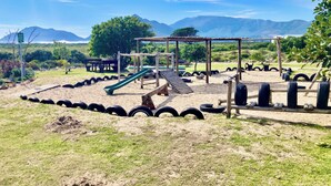 A playground with a slide, swings, and tire obstacles. - Kommetjie Luxury Retreat for Families & Groups (Cape Town)