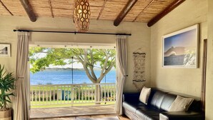 A living room with a view of the sea, a black leather sofa, a patterned rug, and a macrame wall hanging. - Kommetjie Luxury Retreat for Families & Groups (Cape Town)