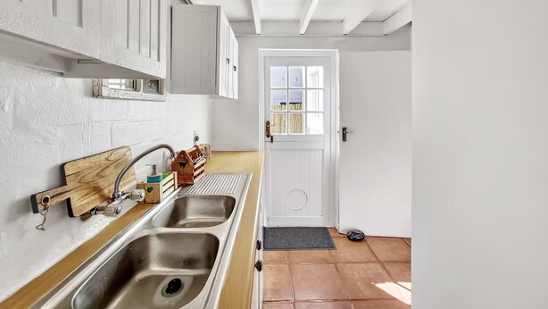 A kitchen with a double sink, wooden utensils, and a window with blinds. - Kommetjie Luxury Retreat for Families & Groups (Cape Town)