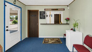 Zona de recepción con alfombra azul, un mostrador, una silla roja y un cartel de bienvenida.