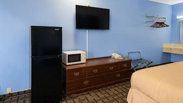 A hotel room with a bed, a dresser, a microwave, a refrigerator, a telephone, and a television mounted on the wall.