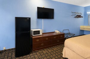 Habitación de hotel con cama, cómoda, microondas, refrigerador, teléfono y televisión montada en la pared.