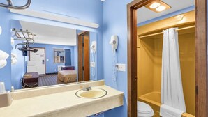 Baño de hotel con lavamanos, espejo, secador de pelo y ducha.
