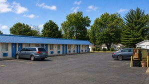 Un motel con una fila de habitaciones, un estacionamiento y un coche estacionado al frente.