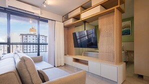 Een moderne woonkamer met een bank, een televisie op een houten dressoir en een stadsgezicht door grote ramen.