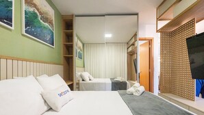 Een hotelkamer met een bed, een extra bed, een televisie, een kledingkast en een schilderij aan de muur.