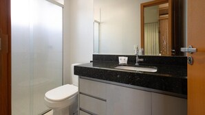 Een badkamer met een glazen douchecabine, een wit toilet, een zwarte marmeren wastafel en een spiegel met houten lijst.