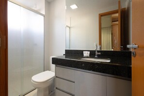 Ein Badezimmer mit Duschkabine aus Glas, einer weißen Toilette, einem schwarzen Marmorwaschbecken und einem Spiegel mit Holzrahmen.